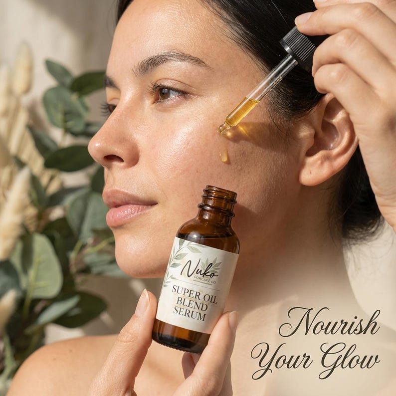 May include: A brown glass bottle of Nuko Skincare Co. Super Oil Blend Serum with a black dropper cap. The label features green leaf illustrations and the text Super Oil Blend Serum. A golden liquid drop is suspended from the glass pipette.