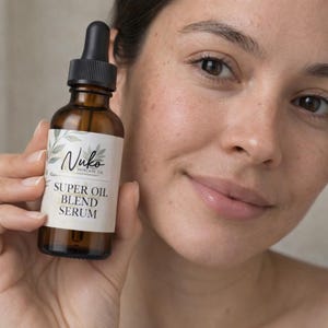 May include: An amber glass dropper bottle containing facial serum with a white label. The label features green leaf illustrations and black text that reads Nuko Skincare Co. Super Oil Blend Serum. The bottle has a black dropper cap.