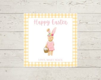 May include: A white card with a yellow gingham border. The card features a cartoon bunny wearing a pink dress and a flower crown. The bunny is holding a basket of colorful eggs. The card says "Happy Easter" and "Love, Mary Mack".