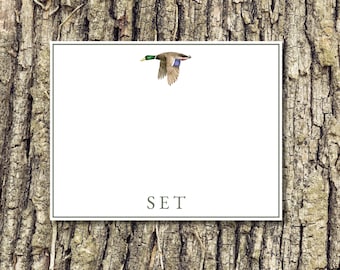 May include: A white card with a green border and the word "SET" in gray text. A watercolor illustration of a flying duck with green, brown, and blue feathers is in the upper right corner. The background is a textured wood.