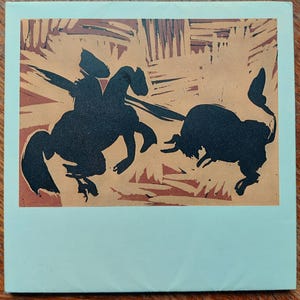 Peut inclure: Une impression carrée présentant la silhouette noire d'une personne montant un cheval et d'un taureau sur un fond beige avec des coups de pinceau texturés brun foncé. L'image est encadrée par une large bordure vert menthe clair.