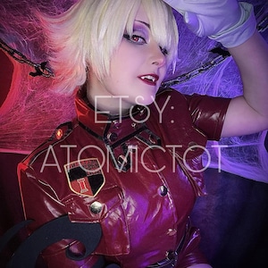 May include: A person in a red cosplay outfit with a matching jacket and shorts. The outfit has a military style with a black and red patch. The person is wearing a blonde wig, white gloves, and has dark makeup. The Etsy shop name "ATOMICTOT" is visible.