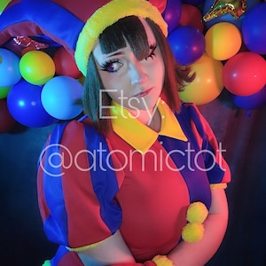 May include: A woman wearing a red, blue, and yellow jester costume with a pointed hat. She is surrounded by colorful balloons and a gold star balloon.