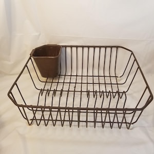 May include: A brown metal dish rack with a rectangular design and vertical dividers for plates. It includes a small, attached brown cup for utensils. The rack is designed to hold dishes after washing.