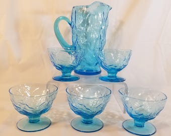 May include: A set of five blue glass pieces, including a pitcher and four small cups. The glass has a textured, frosted look.