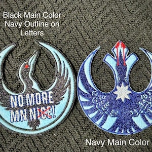 Może przedstawiać: Dwie haftowane naszywki z okrągłym wzorem. Jedna jest czarna z granatowym obrysem i napisem "NO MORE MN NICE!". Druga jest granatowa z jasnoniebieskim wzorem. Obie mają emblemat przypominający ptaka.