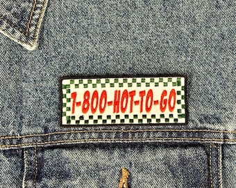 Pode incluir: Uma jaqueta de ganga com um remendo xadrez preto e verde que diz "1-800-HOT-TO-GO" em letras vermelhas.