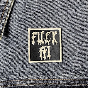 May include: A black and white embroidered patch with the words "FUCK" above "MI" in a gothic font. The patch is sewn onto a blue denim jacket.