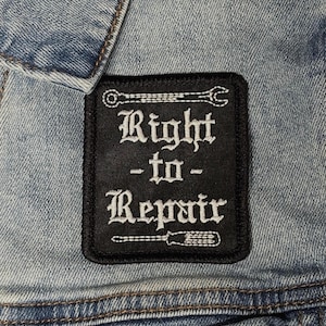 May include: A white ceramic mug with a black handle and the text "But First, Coffee" in a bold, black font. The mug is set against a blurred background, suggesting a cosy setting.