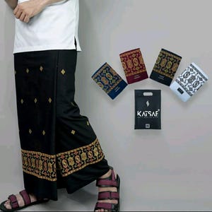 May include: A black sarong with gold and red embroidery. The sarong is folded and displayed with other sarongs in different colours and patterns. The sarongs are packaged in a black bag with the word "Katsaf" printed on it.