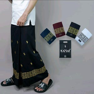 Puede incluir: Un sarong negro con bordados dorados y un patrón geométrico. El sarong lo lleva puesto una persona. Hay cinco sarongs doblados en diferentes colores, incluyendo azul marino, granate, negro y blanco, con el mismo bordado dorado y el mismo patrón geométrico. Una bolsa negra con el texto "Katsaf Daily Muslim Wear" está en el centro de la imagen.