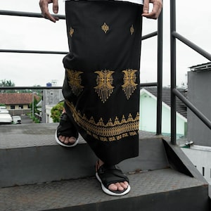 以下が含まれることがあります： 金色の刺繍が施された黒いサロン。デザインは三日月と幾何学模様の繰り返しパターンです。