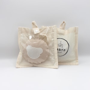 May include: Two beige tote bags. One bag has a clear plastic front with a plush, light brown bear-shaped toy inside. The bear has a white face. The other bag has a black and white logo that says "ABYO baby gifts".