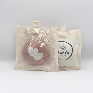 May include: Two canvas tote bags. One bag contains a pink, corduroy, round toy with two white hearts. The toy is visible through a clear plastic window. The second bag has a black and white logo that says "BABYO baby gifts."