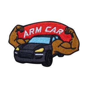 Puede incluir: Un parche bordado que representa un coche negro con una pancarta roja que dice "ARM CAR" encima. El coche está siendo levantado por dos brazos musculosos marrones.