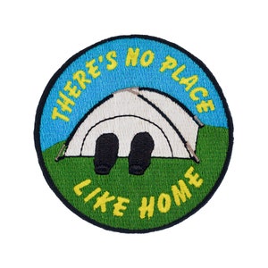 May include: Embroidered patch featuring a blue sky, green grass, and a white tent. The text reads "There's no place like home".