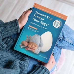 May include: A book titled "Should You Freeze Your Eggs?" is held open, showing a baby illustration and an egg graphic. The cover features text, including "Tailored to you" and "Written by a scientist." The book's cover is blue and orange.