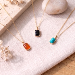 May include: Three gold-tone necklaces, each featuring a single rectangular pendant. One pendant contains an orange stone, one contains a black stone, and one contains a turquoise-colored stone. The chains are thin and delicate, made of gold-tone metal.