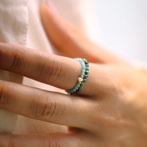 Op de afbeelding: Een close-up van een hand met een ring met turquoise en gouden kralen.