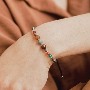 The woman wrist displays this agate and pyrite bead bracelet and its orange chalcedony charm. The green and orange colors and the golden details stand out.