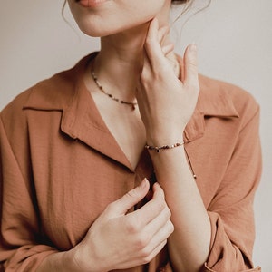 As the woman touches her face with her hand, she wears the red garnet bracelet and matching choker around her neck.