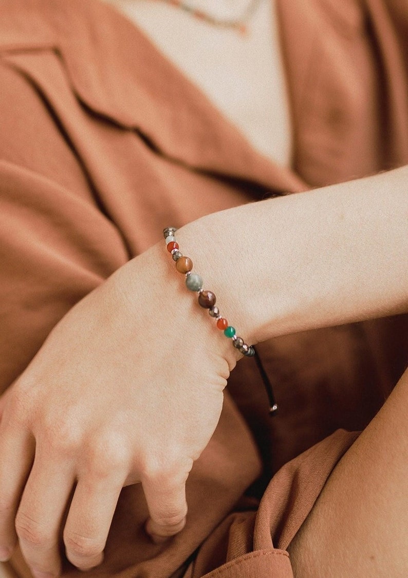 The woman wrist displays this agate and pyrite bead bracelet and its orange chalcedony charm. The green and orange colors and the golden details stand out.