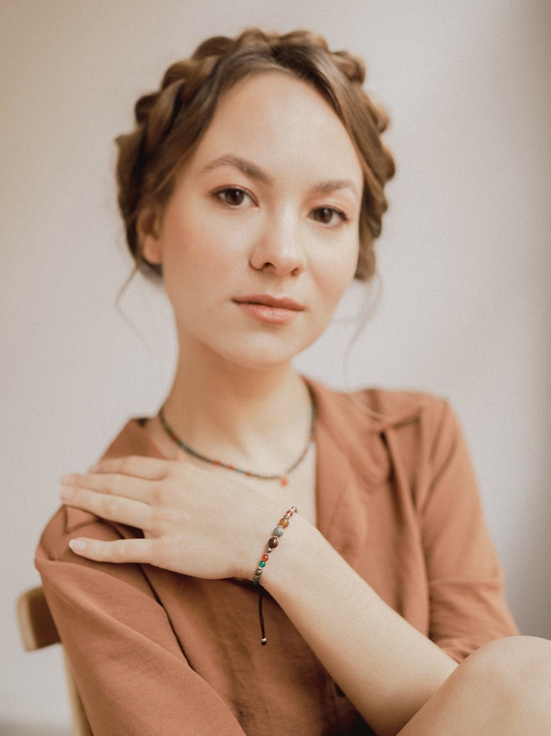 The woman shows off her agate and pyrite bead bracelet combined with orange and boho clothes and her matching choker. The adjustable nylon with gold accents of the bracelet can be seen.