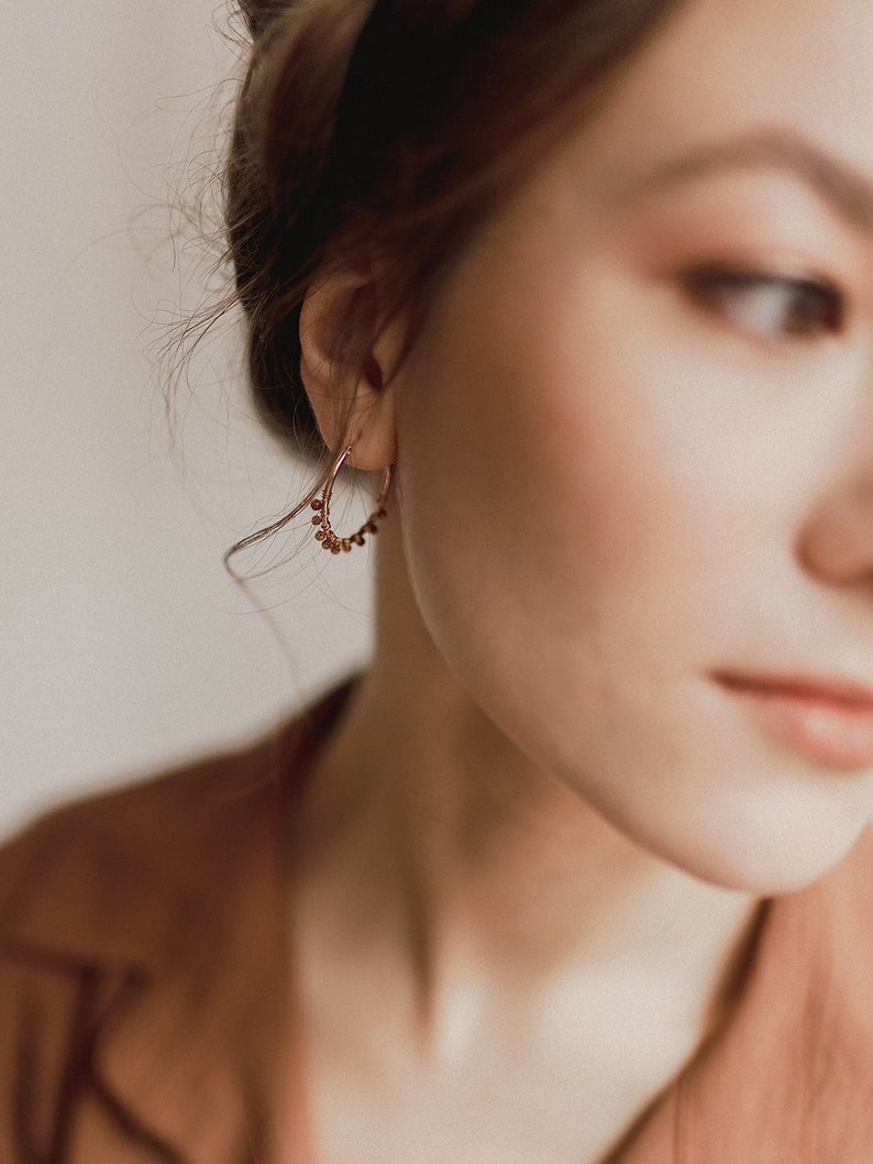 Rose gold plated hoop earrings with aventurine are seen worn on a model standing in profile. Here you can appreciate the size of these earrings, 2.5 cm long.