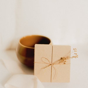 The recycled cardboard box is seen in a minimalist and delicate environment and decorated with tiny dried flowers, ready to make a delicate gift for her.