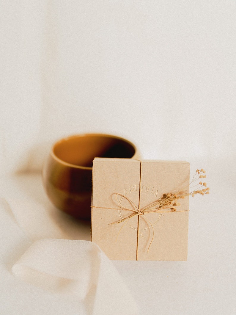 The recycled cardboard box is seen in a minimalist and delicate environment and decorated with tiny dried flowers, ready to make a delicate gift for her.