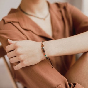 The woman shows off her agate and pyrite bead bracelet combined with orange and boho clothes and her matching choker, also colorful and delicate.