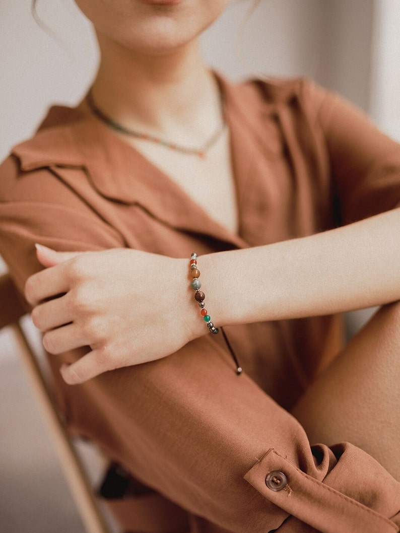 The woman shows off her agate and pyrite bead bracelet combined with orange and boho clothes and her matching choker, also colorful and delicate.