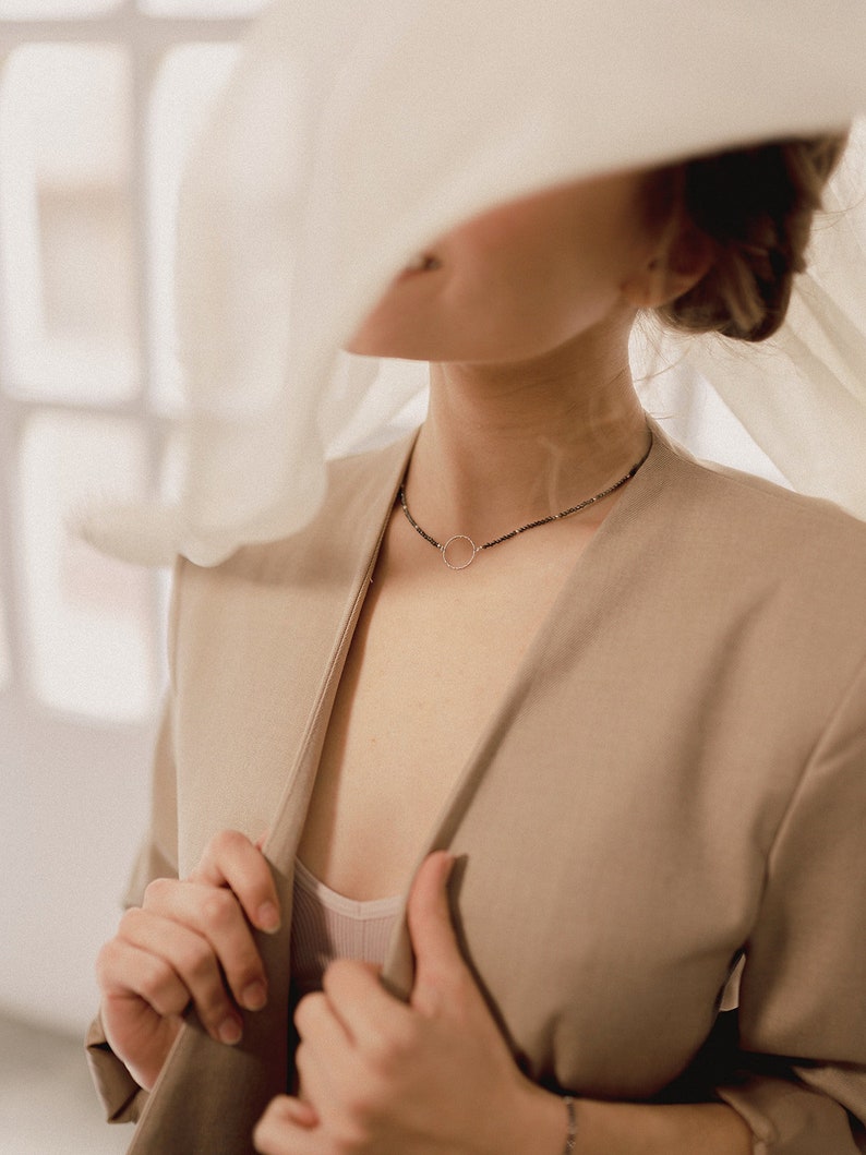 The woman shows her minimalist choker of spinel beads and sterling silver circle from one side, matched with delicate and elegant clothes.