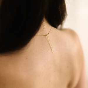 May include: A delicate gold necklace with an adjustable chain is draped across a person's bare back. The necklace's chain extends down the back, creating a simple yet elegant look. The focus is on the jewelry and the skin.