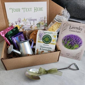 May include: A gift box with a gardening theme, containing a miniature watering can, seed packets, tea, and snacks. A small shovel-shaped spoon with a green ribbon is in the foreground. The box includes a card that says "Your Text Here".