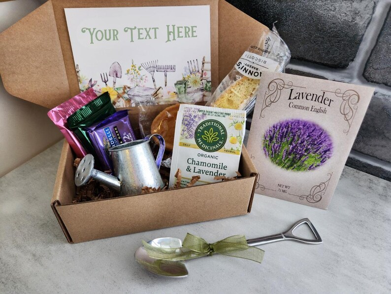 May include: A gift box with a gardening theme, containing a miniature watering can, seed packets, tea, and snacks. A small shovel-shaped spoon with a green ribbon is in the foreground. The box includes a card that says "Your Text Here".