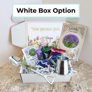 May include: A white gift box labeled "White Box Option" filled with various items. Inside are tea packets, a small watering can, a decorative spoon, and a packet of lavender seeds. A card with the text "Your Message Here" is also included.