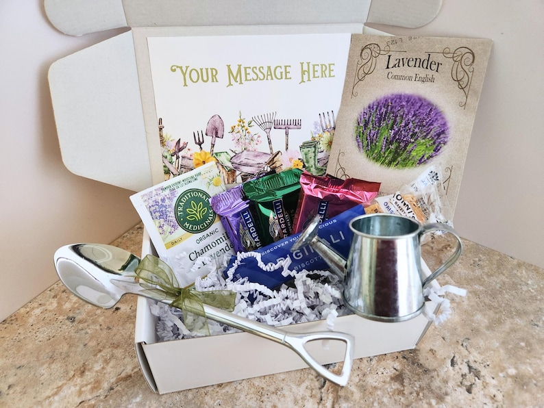 May include: A gift box filled with gardening-themed items. Includes a silver watering can, a large spoon, tea packets, and a packet of lavender seeds. The box also contains a card with the text "Your Message Here".