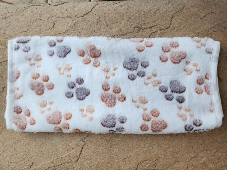 May include: White plush blanket with a brown and gray paw print pattern.