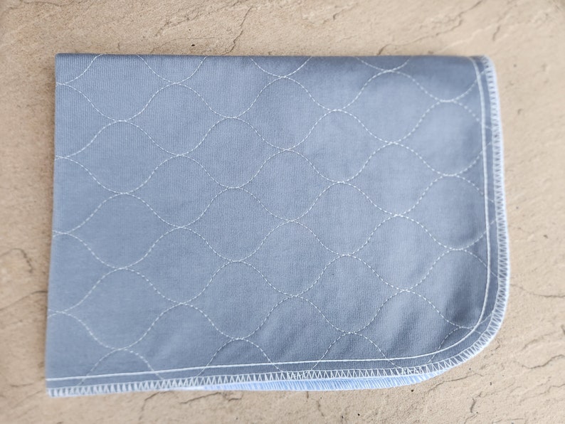 May include: A light blue quilted fabric pad with a white stitched diamond pattern. The pad has a white and blue binding around the edges.