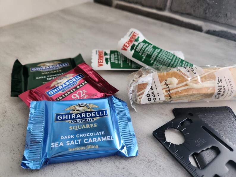 May include: An assortment of packaged snacks and treats, including Ghirardelli chocolate squares in dark chocolate mint, intense dark 92%, and sea salt caramel flavors. Also, a Vermont beef stick and biscotti.