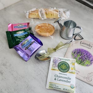 May include: An assortment of treats and tea, including Ghirardelli chocolate squares, a mini watering can, a small pie, and a packet of Chamomile & Lavender tea. A packet of lavender seeds and a serving spoon are also included.