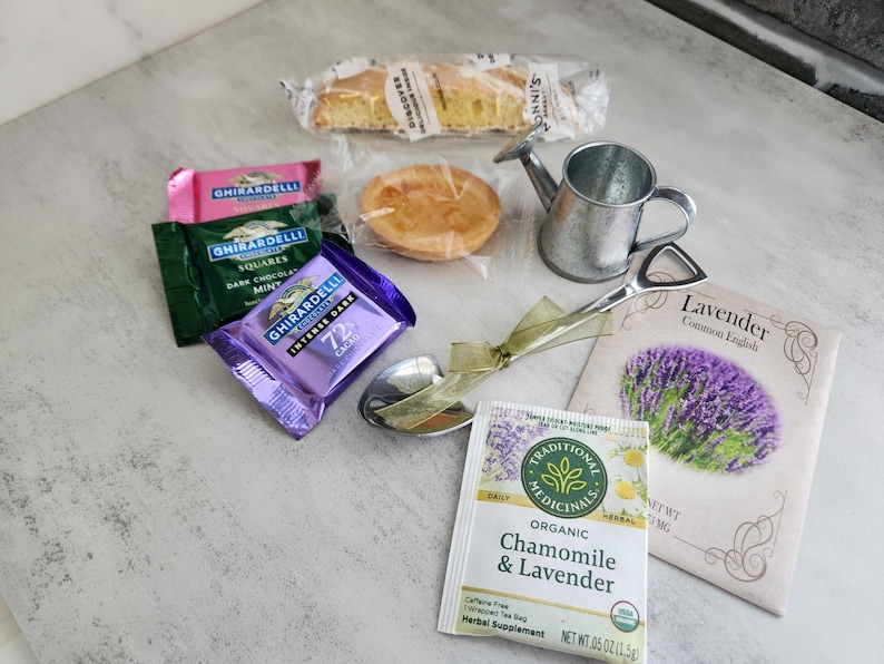 May include: An assortment of treats and tea, including Ghirardelli chocolate squares, a mini watering can, a small pie, and a packet of Chamomile & Lavender tea. A packet of lavender seeds and a serving spoon are also included.