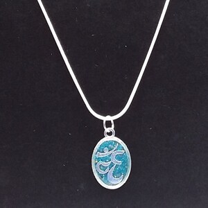 May include: A silver chain necklace with an oval pendant featuring a teal blue Om symbol.