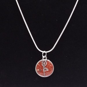 May include: A silver chain necklace with a round pendant featuring a red and brown resin design with a silver yoga pose silhouette.