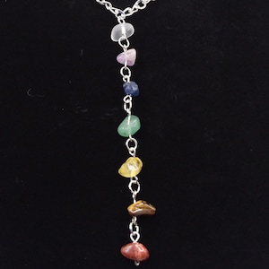 May include: A silver chain necklace with seven different colored stones hanging from it. The stones are clear, pink, blue, green, yellow, brown, and red.