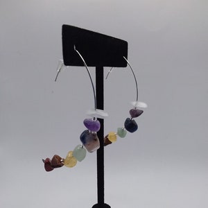 May include: Silver hoop earrings with a rainbow of gemstone beads. The beads are in the order of red, orange, yellow, green, blue, purple, and white.