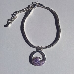May include: A silver chain bracelet with a round pendant featuring a purple wave design.