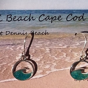 May include: Silver dangle earrings with a turquoise blue wave design. The earrings are labeled "Mi Beach Cape Cod West Dennis Beach" and "by Michele Sullivan".
