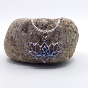 May include: Silver necklace with a lotus flower pendant featuring an Om symbol. The necklace is displayed on a gray rock.